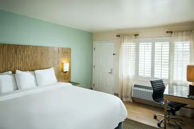 a bedroom with a white bed and a desk and a chair at PB Surf Beachside Inn in San Diego