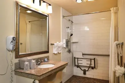 a bathroom with a sink and a shower with a mirror at Lamplighter Inn & Suites at SDSU in San Diego