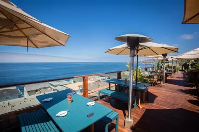 a deck with tables and umbrellas and the ocean at La Casa Del Camino in Laguna Beach