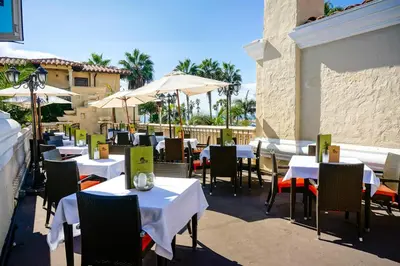 a restaurant with white tables and chairs and umbrellas at Balboa Inn, On The Beach At Newport in Newport Beach