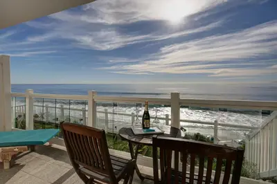 a table with a bottle of wine on a balcony with the ocean at Capri Laguna on the Beach - A Boutique Hotel in Laguna Beach