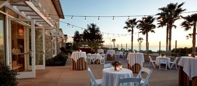 a restaurant with white tables and chairs and palm trees at Cape Rey Carlsbad Beach, A Hilton Resort & Spa in Carlsbad