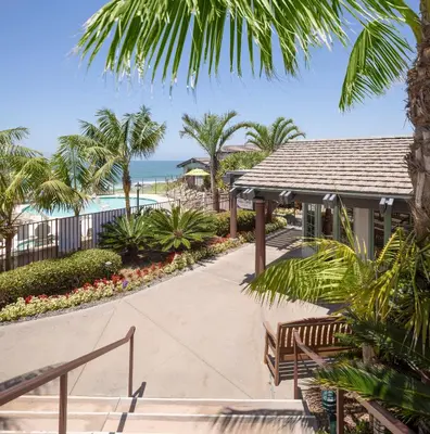 a walkway leading to a resort with a pool and palm trees at WCH at Wave Crest Resort in Del Mar