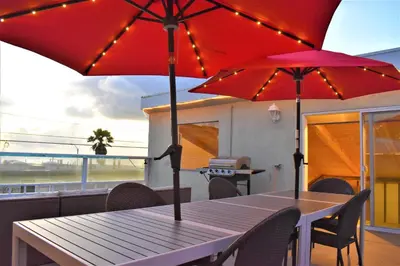 a wooden table with two red umbrellas on a balcony at Luv Oceanside Views-1 House to Beach, Boardwalk and Waves-Spacious Rooftop Sun Deck-Plus King Beds too! in San Diego