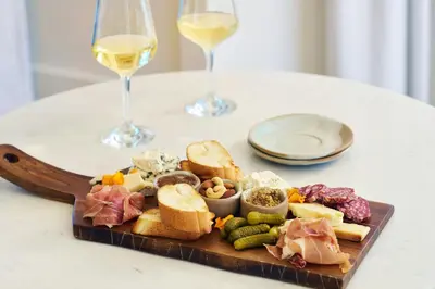 a plate of food on a table with two glasses of wine at Tiller House, Laguna Hills, a Tribute Portfolio Hotel in Laguna Hills