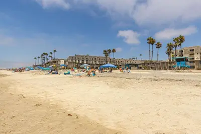 a beach with people sitting under blue umbrellas at Penthouse Condo w/ Panoramic Ocean Views at Beach Resort in Oceanside