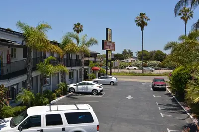 a parking lot with parked cars and palm trees at Harbor Inn & Suites Oceanside in Oceanside