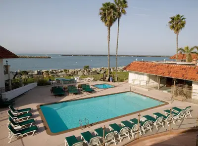 a swimming pool with chairs and the ocean in the background at Oceanside Marina Suites - A Waterfront Hotel in Oceanside