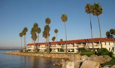 a building with palm trees in front of the water at Oceanside Marina Suites - A Waterfront Hotel in Oceanside