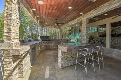 an outdoor kitchen with a stone wall and stools at El Cajon Home with Pool, Grill Station and Decks in El Cajon