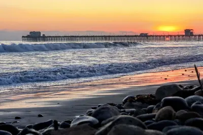a beach at sunset with a pier in the background at Oceanside Home with Yard - Walk to Beach and Pier in Oceanside