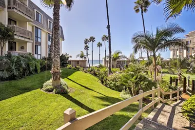 a resort with palm trees and a white fence at Beachfront Oceanside Condo with Pool and Hot Tub! in Oceanside