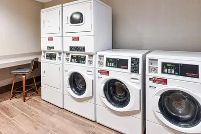 a laundry room with three washing machines and a chair at Fairfield Inn & Suites by Marriott Menifee in Menifee