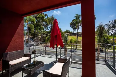 a patio with two chairs and a red umbrella at Cute Studio With Large Balcony and Great Park View in San Diego