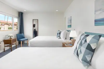 a bedroom with two beds and a desk with a chair at Pacific Edge Hotel in Laguna Beach