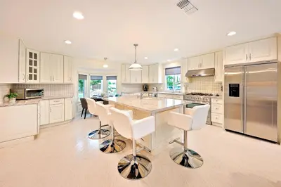 a kitchen with white cabinets and a island with bar stools at Enchanting Cottage By the Sea in Carlsbad
