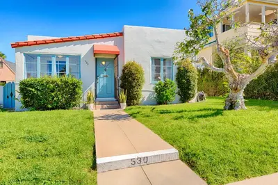 a house with a blue door on a green lawn at Seashell Cottage in San Diego