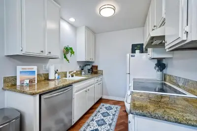 a kitchen with white cabinets and a sink and a refrigerator at 90 Walk Score - Steps to Beach & Dining - Reserved Parking in Carlsbad
