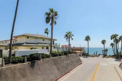 a street in front of a house with palm trees and the ocean at The Bridge At South Oceanside is the Perfect Family Beach House now with AC in Oceanside