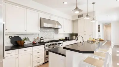 a white kitchen with white cabinets and black counter tops at Crystal Cove by AvantStay Gorgeous Charming Newport Home in Newport Beach