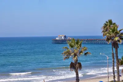 a beach with palm trees and a pier at Fantastic Ocean View Remodeled All New Furnishings Pet Friendly AC in Oceanside