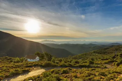 a house in the mountains with the sun in the sky at A LIVING CANVAS Amazing Lake View Custom Home in Julian