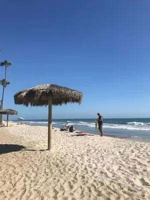 a beach with a straw umbrella and people on the beach at Blue Whale Inn San Clemente Charmer Unit A in San Clemente