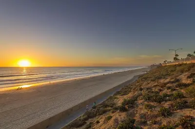 a beach with the sun setting in the ocean at Luxury Ocean Views & Steps To The Sand - Tower 36 Upper Condo Unit in Carlsbad