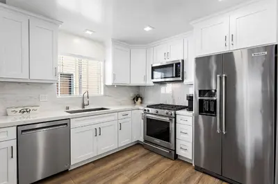 a kitchen with white cabinets and a stainless steel refrigerator at Amazing New & Water Vu/Balboa Peninsula! EV charge in Newport Beach
