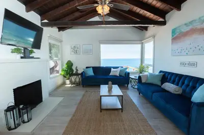 a living room with a blue couch and a tv at OCEAN FRONT Beach HOUSE! Private Stairs to SAND! in Laguna Beach