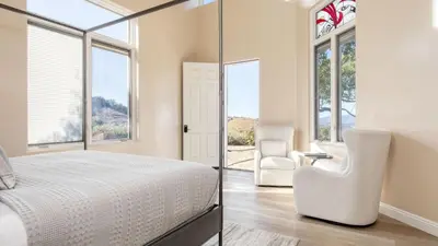 a bedroom with a bed and a chair and windows at Modern Temecula Mansion w Pool Hot Tub Guest House Valley Views Camila by AvantStay in Temecula