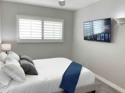 a white bedroom with a bed with a tv on the wall at Steps To The BEST Beach . Surf . Spa . Main Street in Encinitas