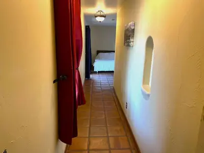 a hallway with a room with a bed and a red door at Private Home on 10 Acres - Heated Salt Pool & Jacuzzi, Mountain & City Views, Horseshoes, Basketball, BBQ, Golf Putting, Foosball, Croquet, Bose Stereo, White Cotton Bedding - Hilltop Hacienda, Pool Heat Optional in Jamul