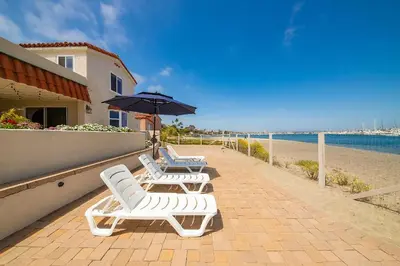 three white chairs and an umbrella on a sidewalk next to the beach at On The Beach Casa in San Diego