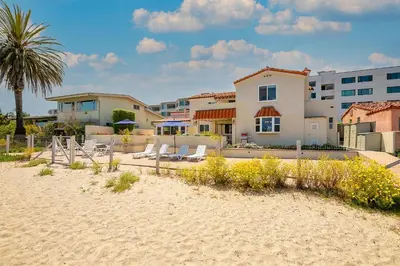 a beach with chairs and a house and a palm tree at On The Beach Casa in San Diego