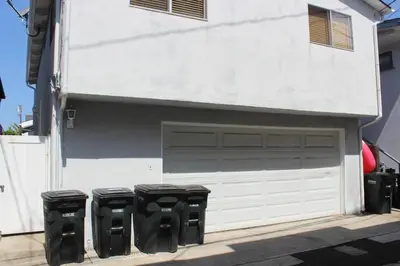 a white garage with three trash cans next to it at 210 Opal Ave Front House in Newport Beach