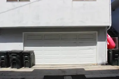 a white garage door with two black trash cans at 210 Opal Ave Front House in Newport Beach